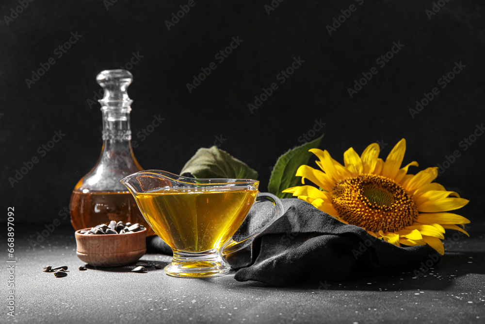 Gravy boat of sunflower oil and wooden bowl with seeds on black background