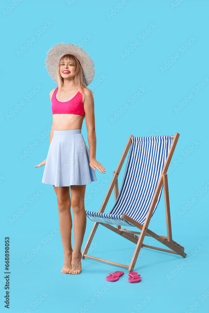 Young woman dressed as doll and deck chair on blue background