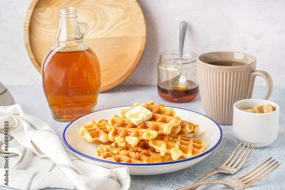 Plate of tasty waffles with maple syrup on white background