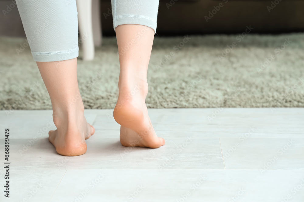 Barefoot woman on floor with heating at home, back view