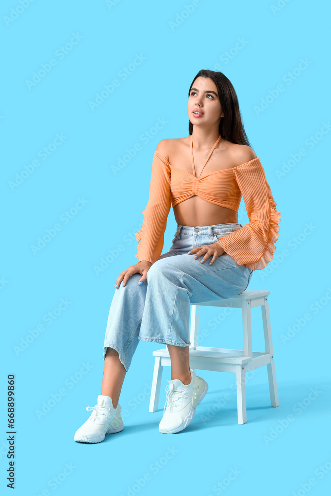 Beautiful young woman sitting on chair against blue background