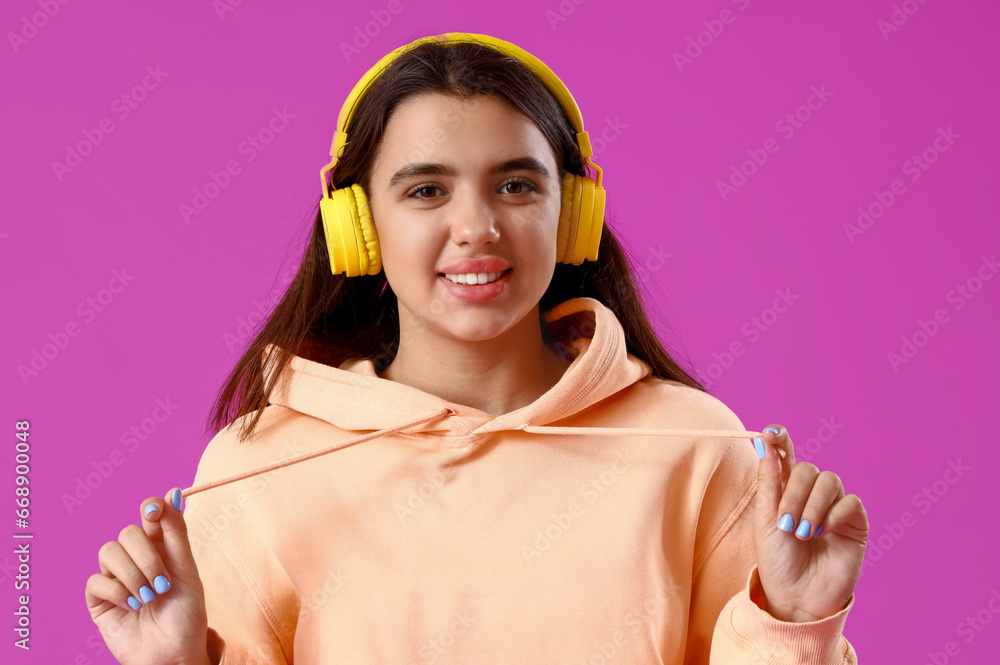 Beautiful young woman in stylish hoodie and headphones on purple background