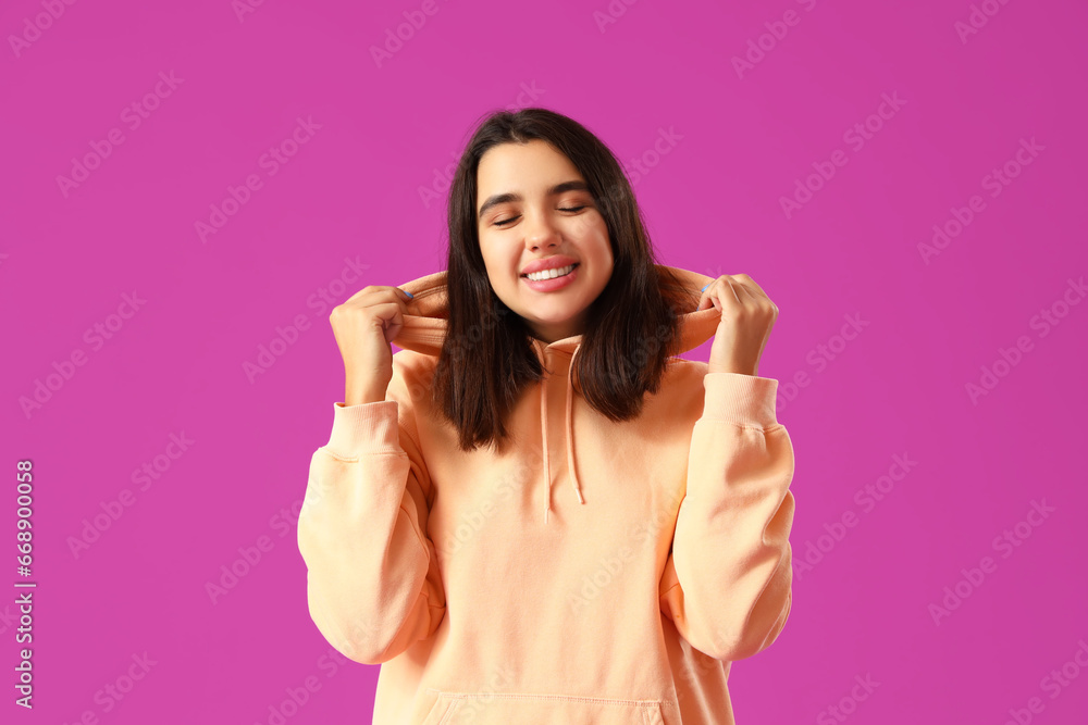 Beautiful young woman in stylish hoodie on purple background