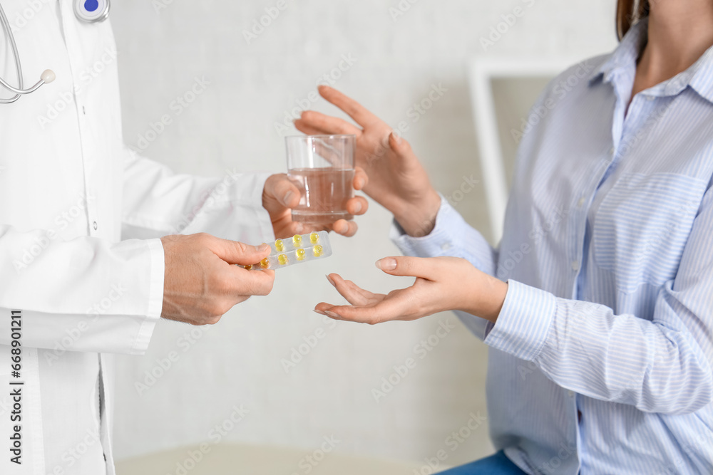 Male doctor giving pills and water to pregnant woman in clinic, closeup