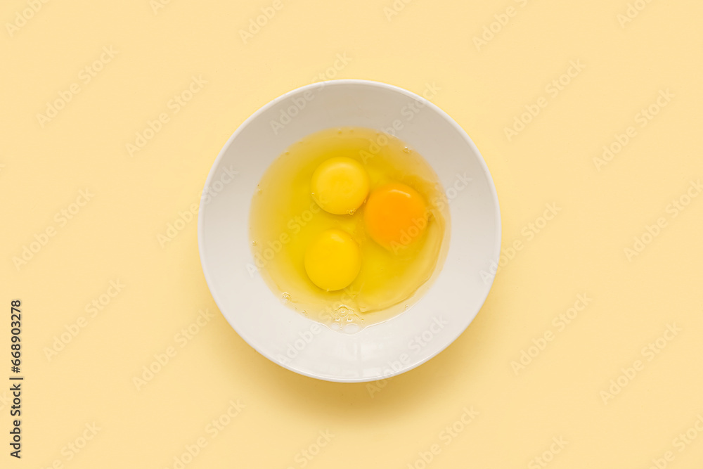 Bowl with cracked chicken eggs on yellow background