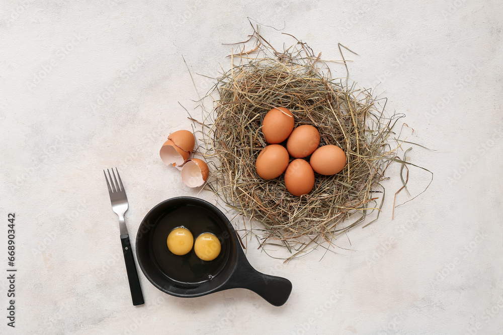 Frying pan and nest with fresh chicken eggs on white background