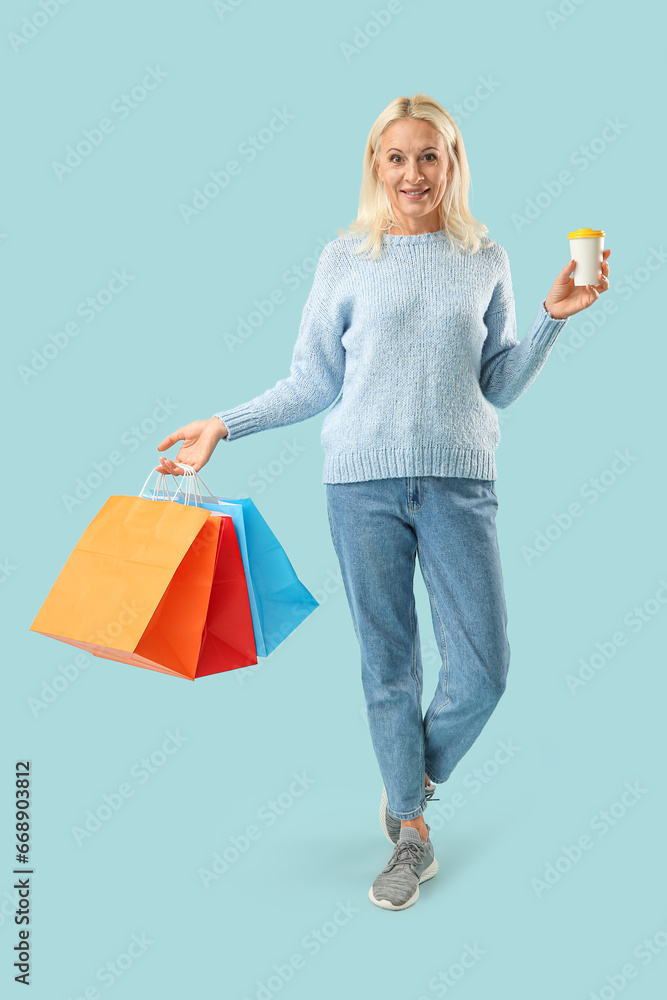 Mature woman with takeaway cup of coffee and shopping bags on blue background