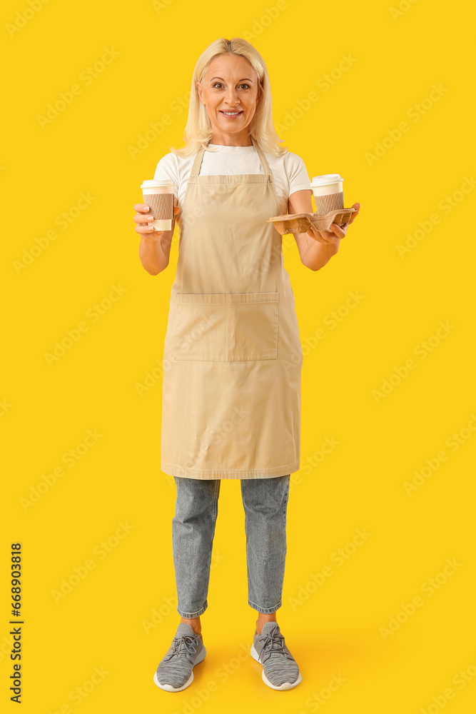 Mature woman with cups of coffee on yellow background