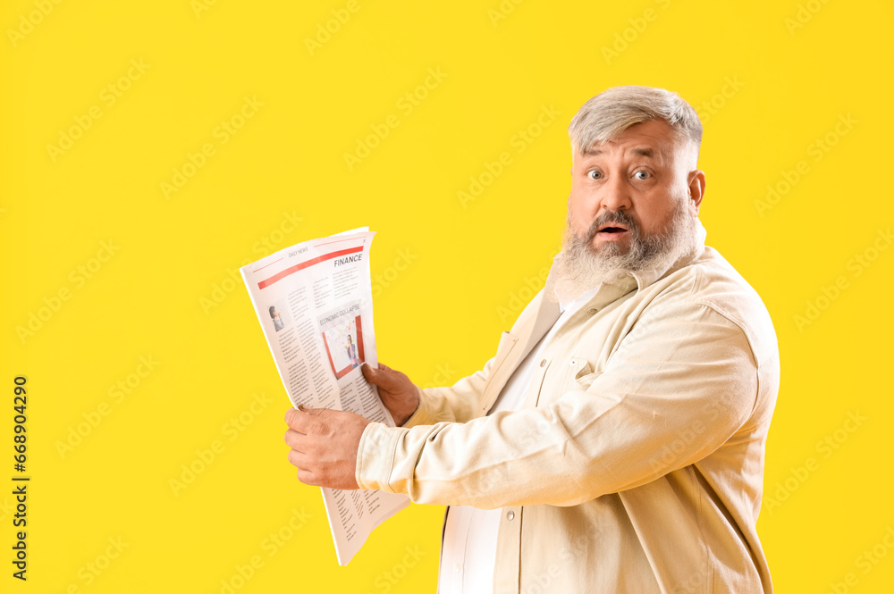 Mature shocked man with newspaper on yellow background