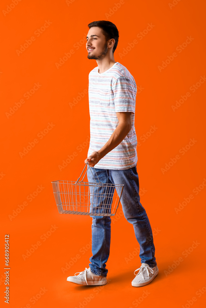 Young man with shopping basket on orange background