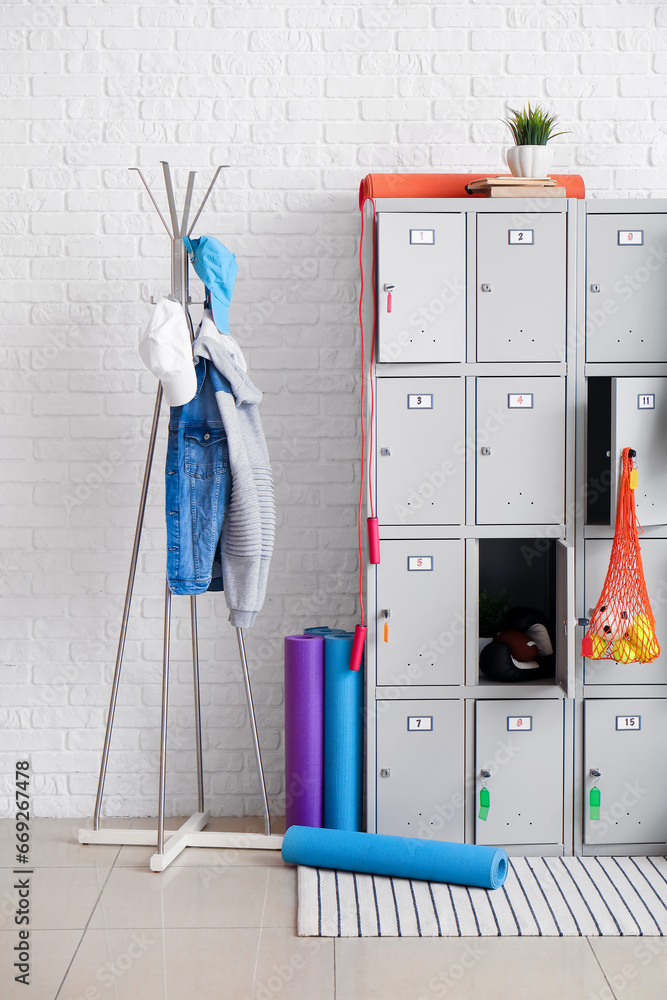 Modern locker with sports equipment and rack near white brick wall