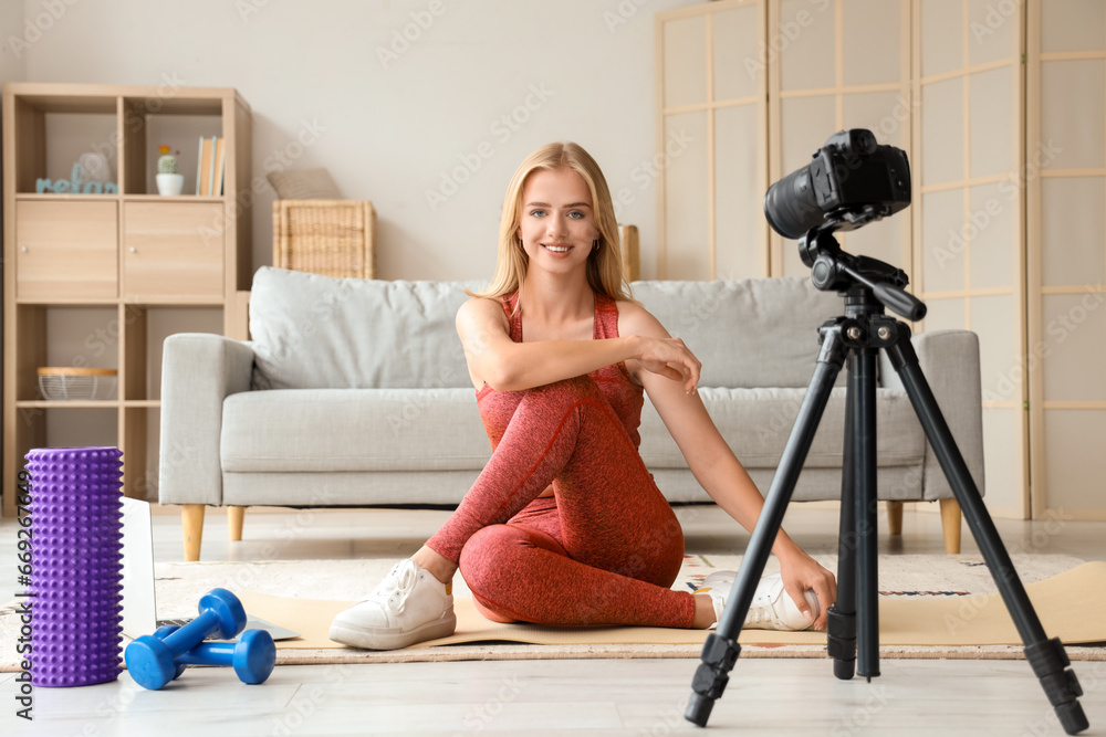 Beautiful young sport blogger recording video while training with roller and dumbbells at home