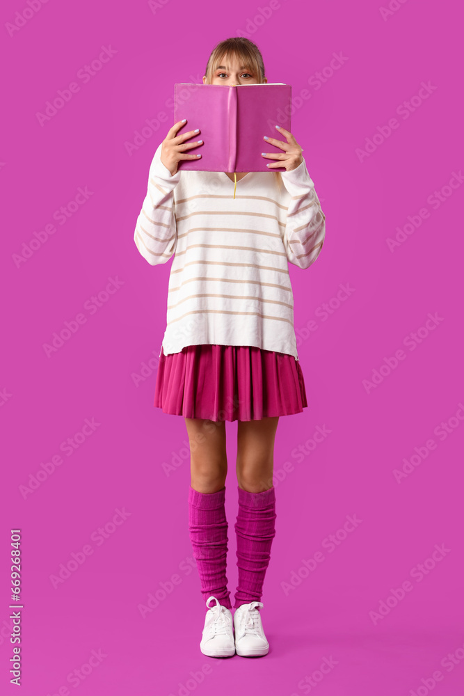 Young woman dressed as doll with book on purple background