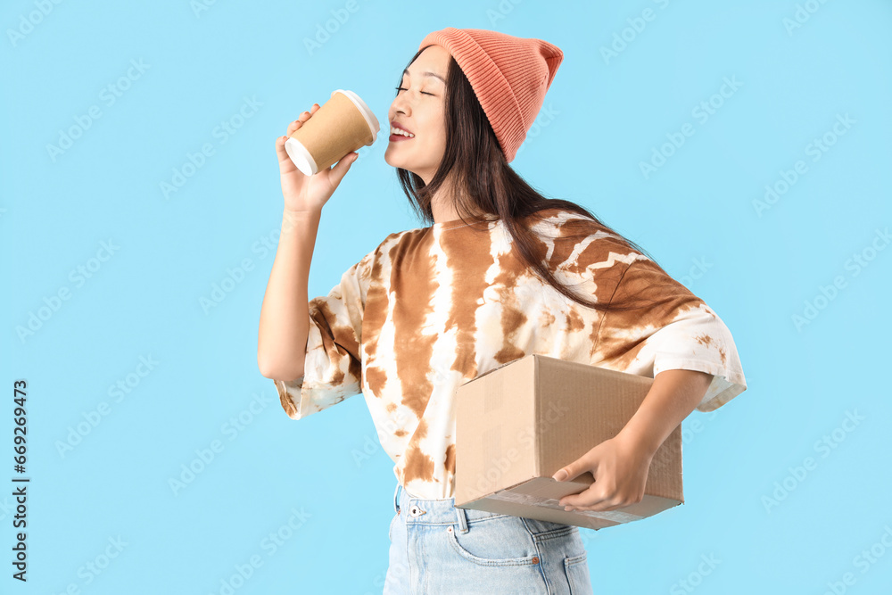 Young Asian woman with parcel and coffee cup on blue background