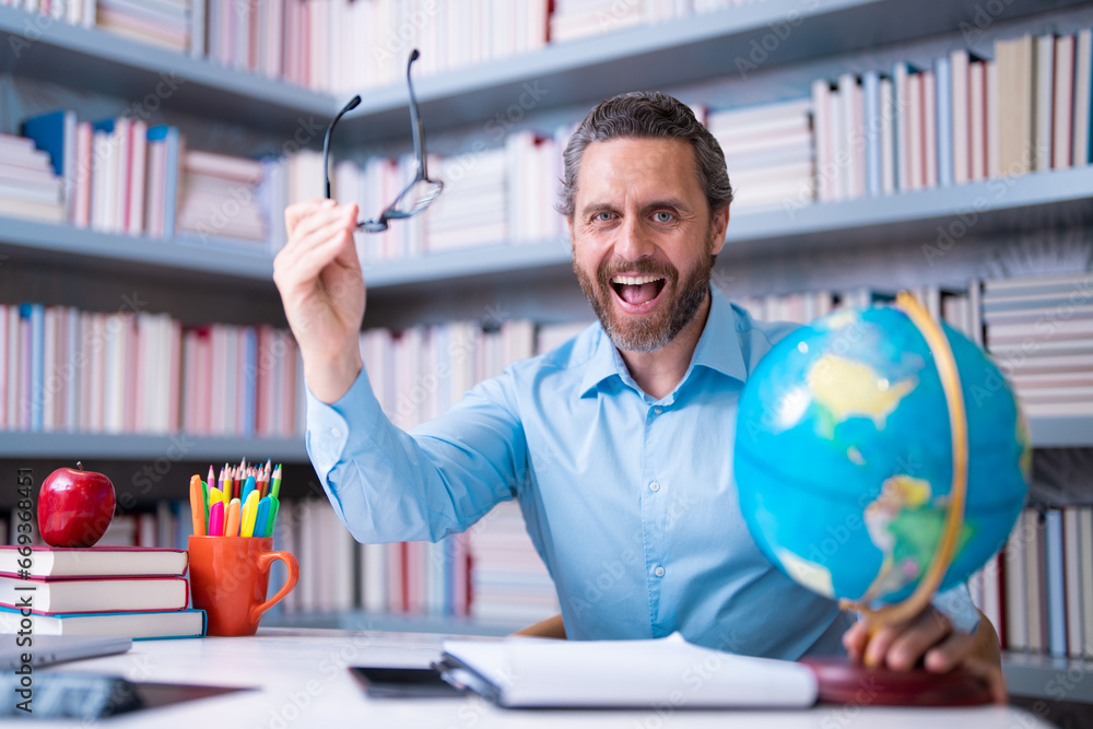 Portrait of teacher with book in library classroom. Handsome teacher in university library. Teachers Day. Teacher giving classes. School teacher in library. Tutor at college library on bookshelf.