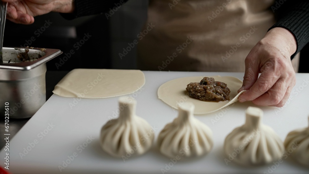 Womens hands make manti, khinkali, dumplings from dough with meat filling. Homemade food. Close-up of a chef preparing dough with minced meat. Hands form tortellini.