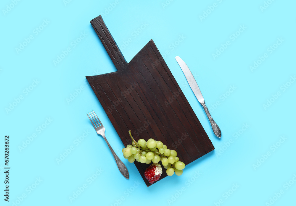 Composition with wooden cutting board, fruits and cutlery on color background