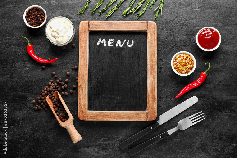 Composition with blank menu board, spices, sauces and cutlery on dark background