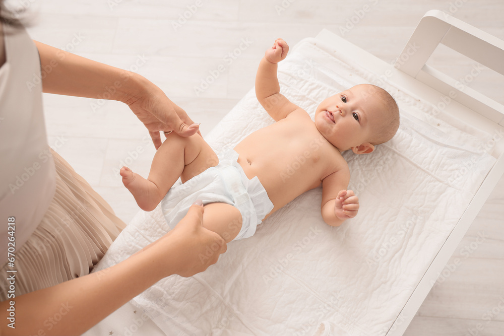 Mother with little cute baby in diaper on changing table at home