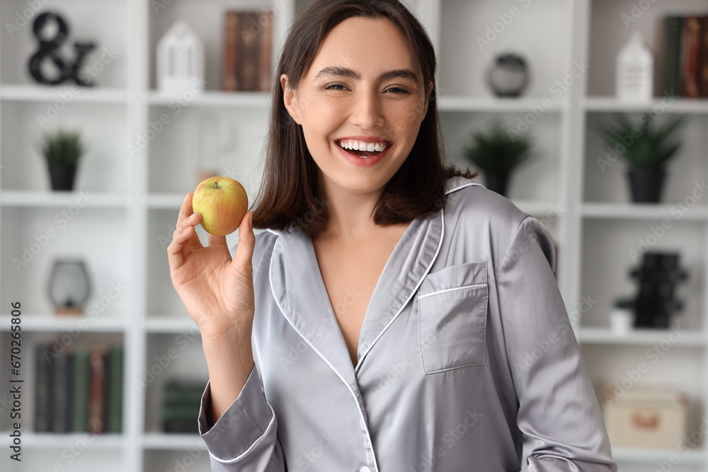 Beautiful young woman with fresh apple in living room at home