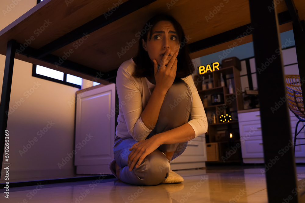 Beautiful young afraid woman under table in evening at kitchen