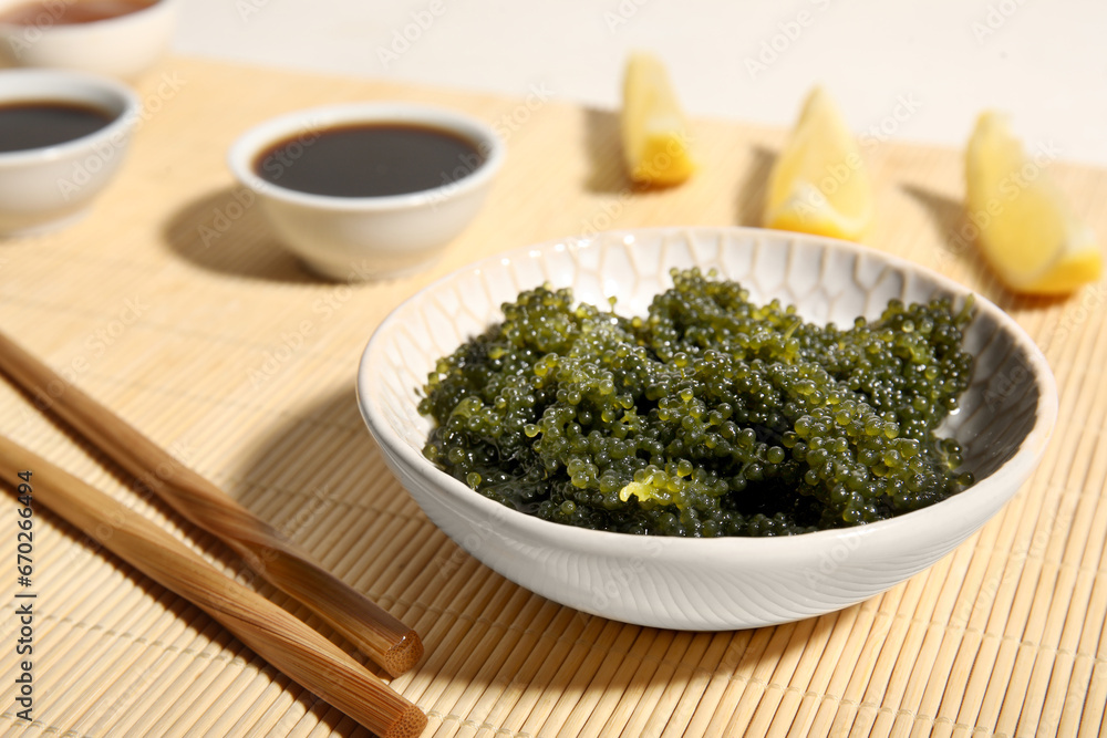 Bowl with healthy seaweed, soy sauce and lemon slices on bamboo mat, closeup