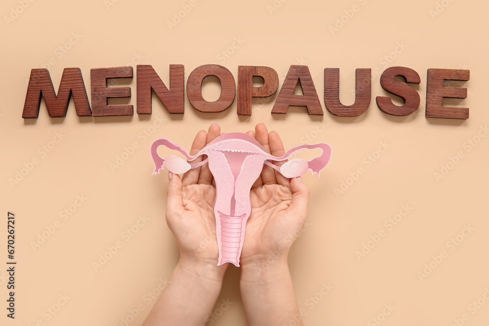 Woman with paper uterus and word MENOPAUSE on beige background