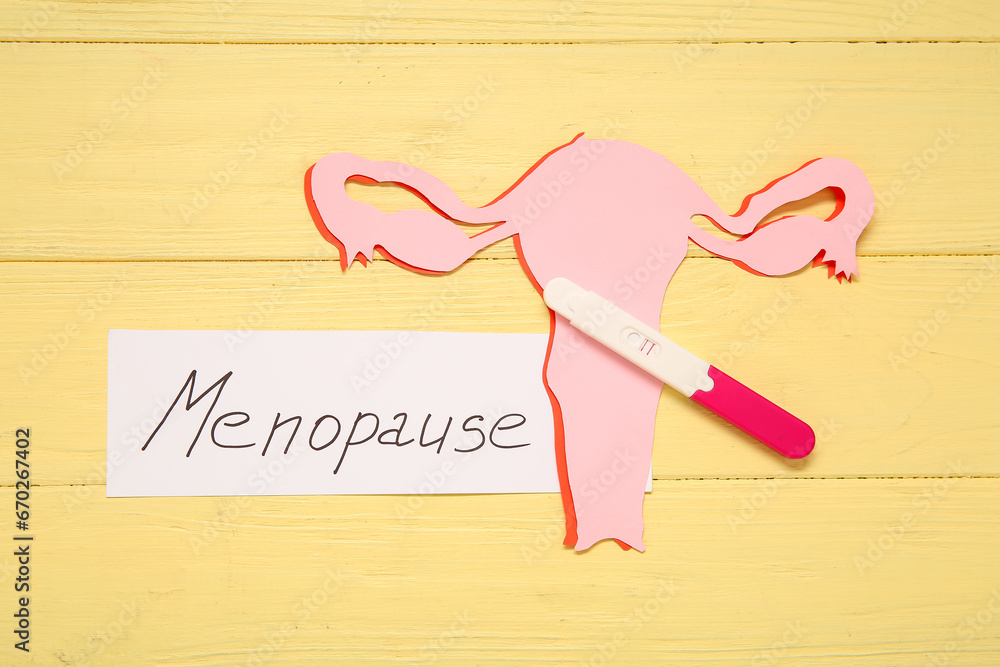 Word MENOPAUSE with paper uterus and pregnancy test on yellow wooden background