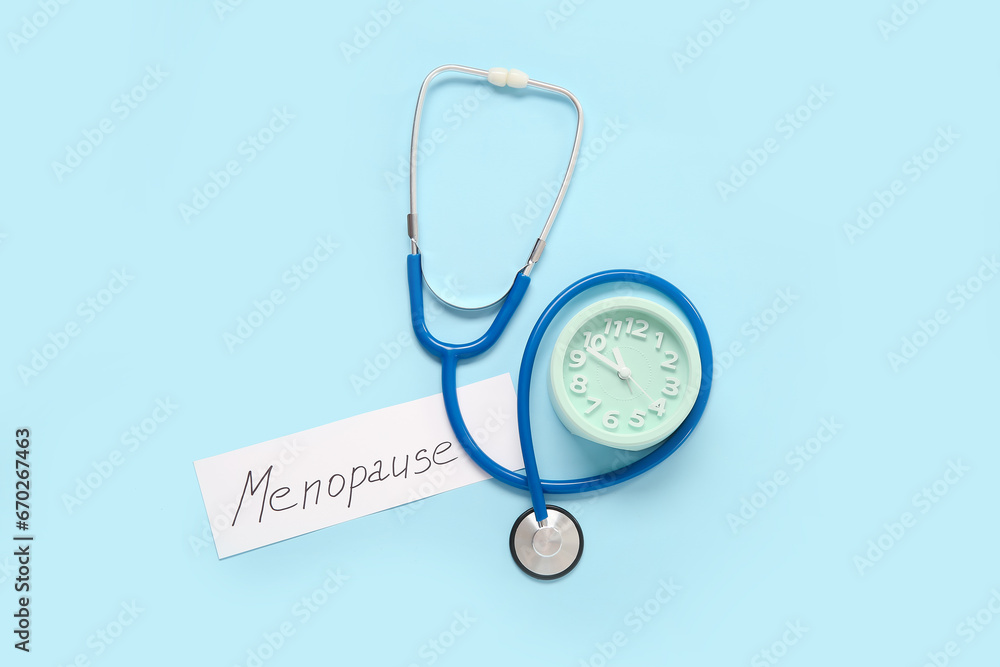 Word MENOPAUSE with stethoscope and clock on blue background