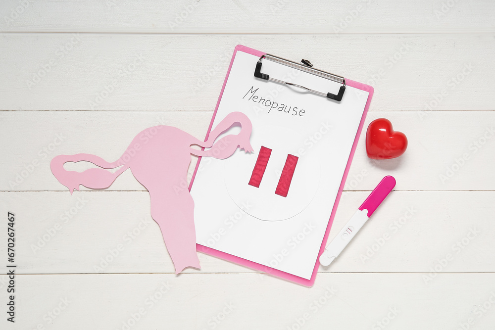 Clipboard with word MENOPAUSE, paper uterus, heart and pregnancy test on white wooden background