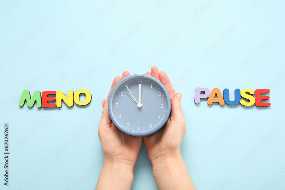 Woman with alarm clock and word MENOPAUSE on blue background