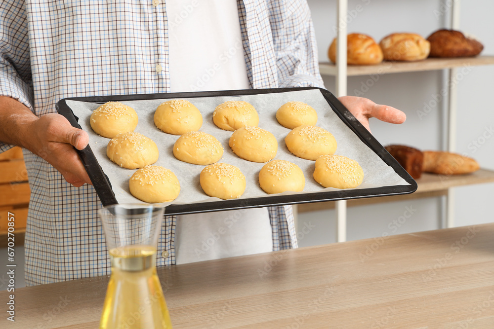 Handsome young man holding tray with fresh raw buns in bakery