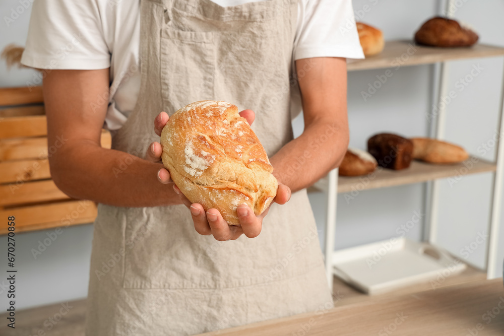 Handsome young man with loaf of fresh bread in bakery