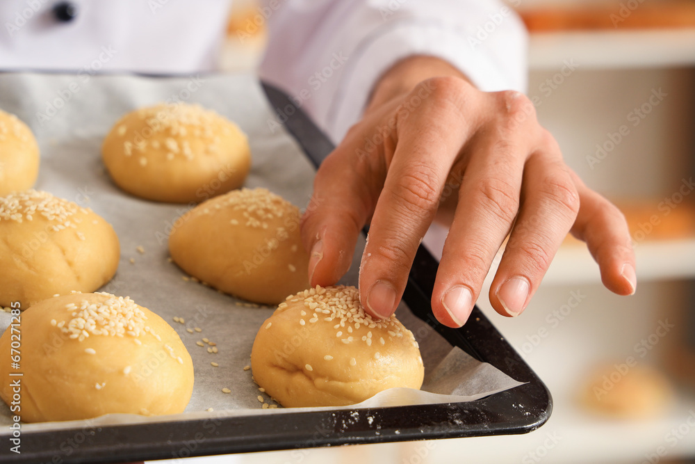 Handsome young chef with tray of fresh raw buns in bakery