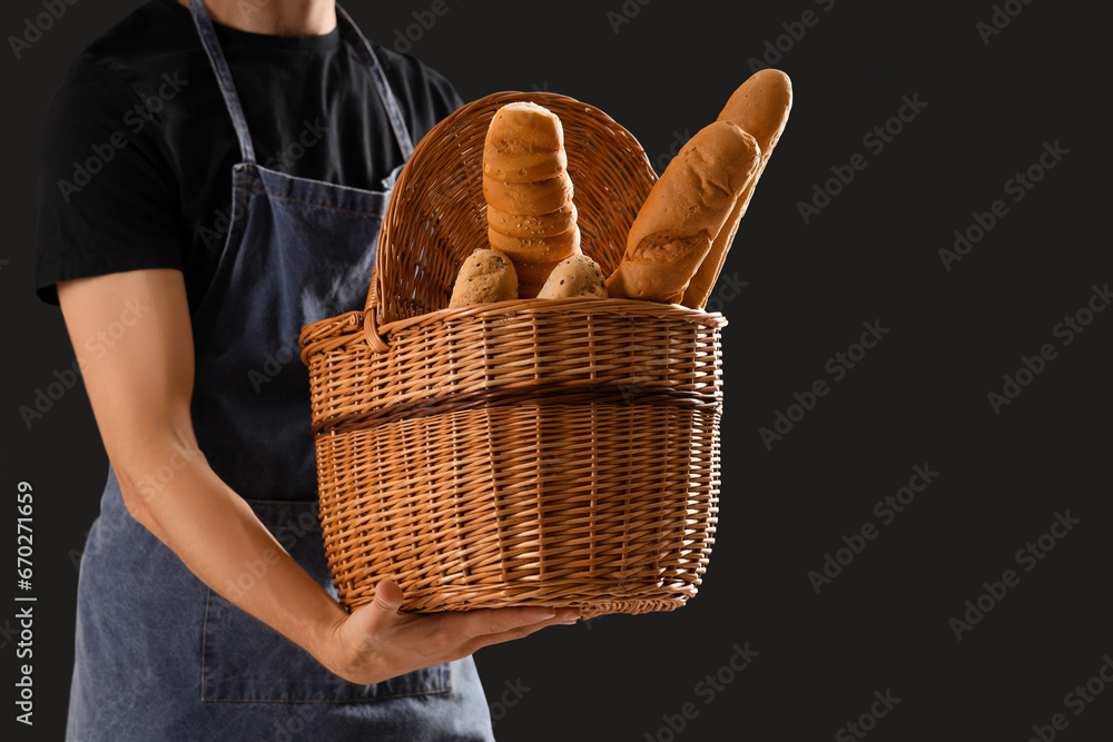 Handsome young man with basket full of fresh baguettes on black background