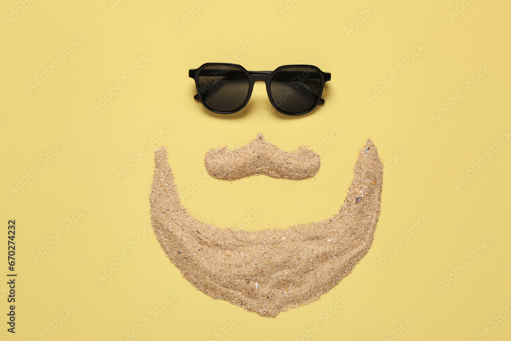 Funny face made of sand and stylish sunglasses on color background