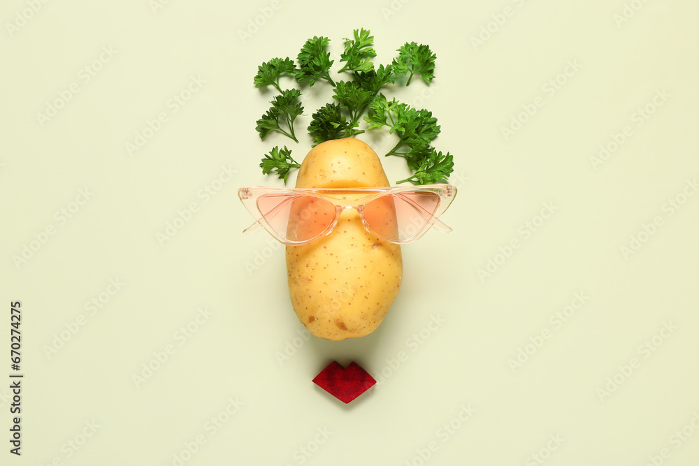 Funny face made of potato, parsley and sunglasses on color background