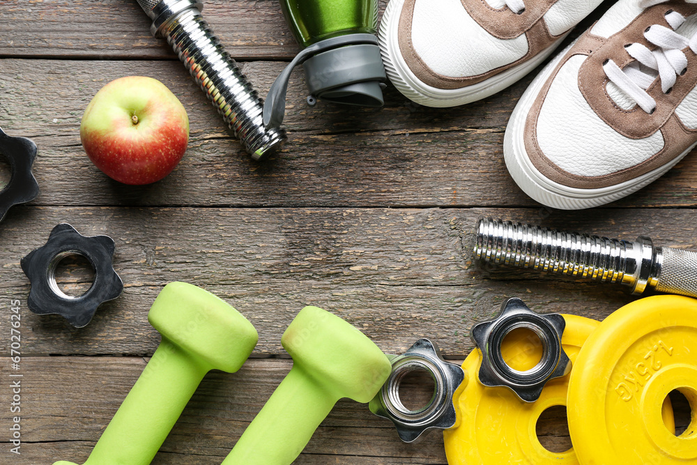 Frame made of barbell plates, apple, shoes, grip and clamps on wooden background