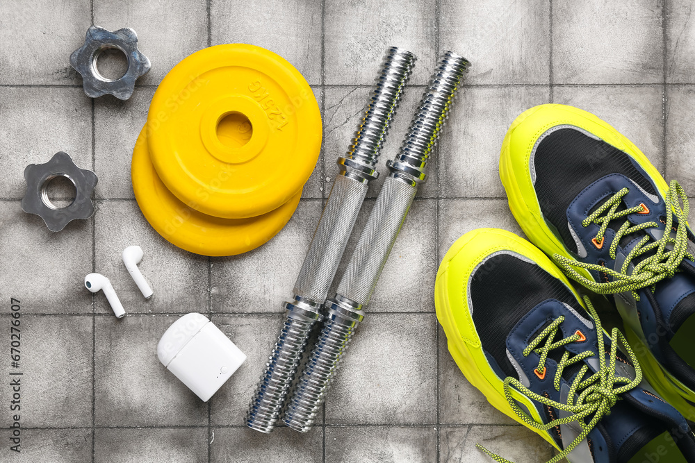 Barbell plates, shoes, grips, earphones and clamps on grey tile background