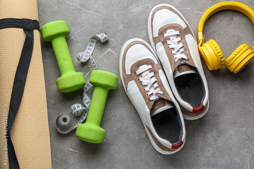 Dumbbells, shoes, headphones, yoga mat and measuring tape on grey background