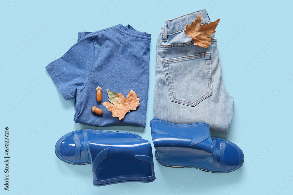 Blue gumboots with t-shirt, jeans and autumn leaves on color background