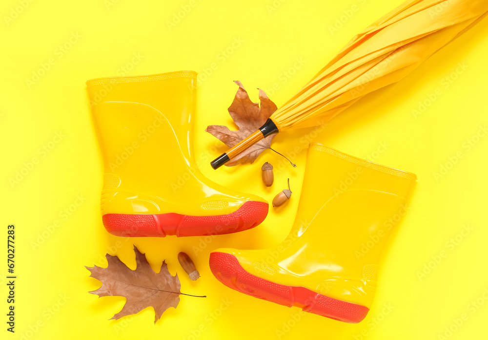 Yellow gumboots with umbrella, acorns and autumn leaves on color background