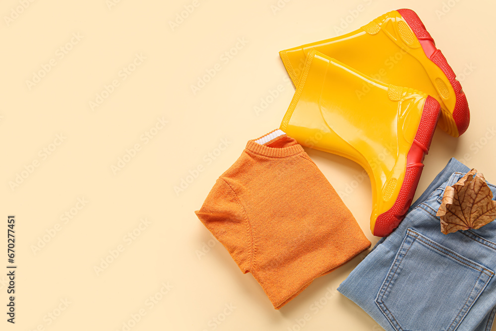 Yellow gumboots with sweater, jeans and autumn leaf on color background