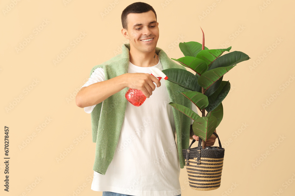 Young man with plant and spray water bottle on beige background