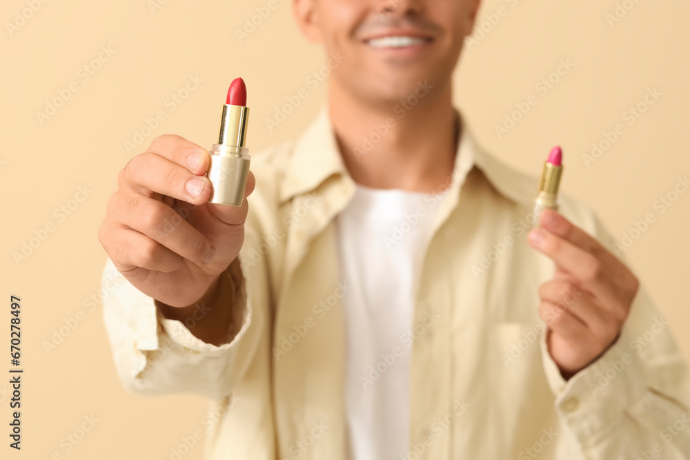 Male makeup artist with lipsticks on beige background, closeup