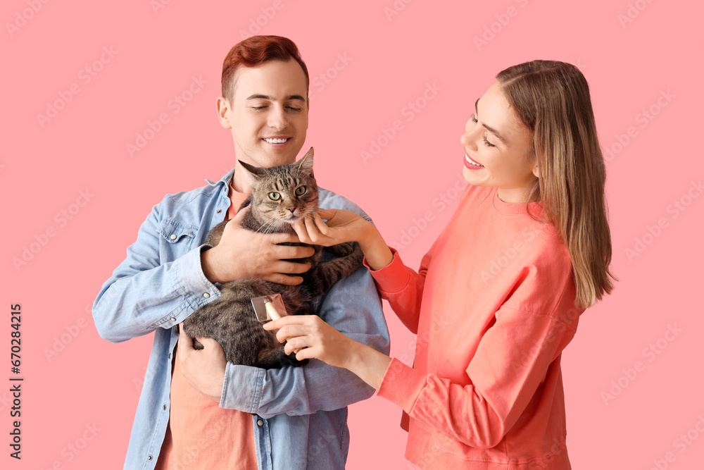 Young couple with cute cat on pink background