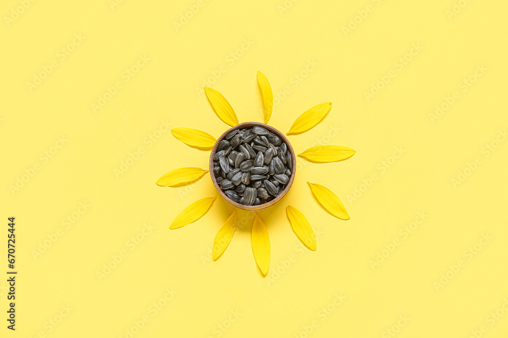 Sunflower petals and bowl with seeds on yellow background