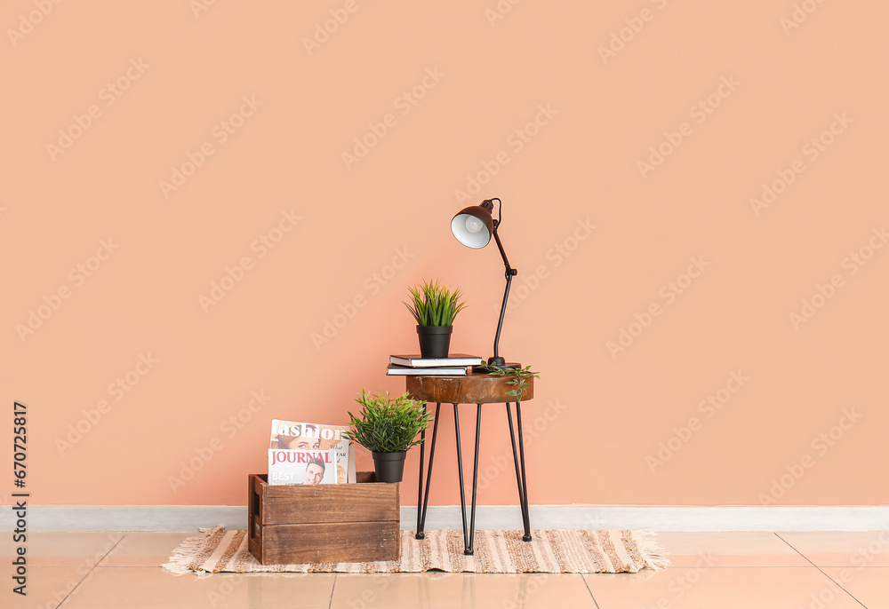 Desk lamp and houseplant on small wooden table near pink wall