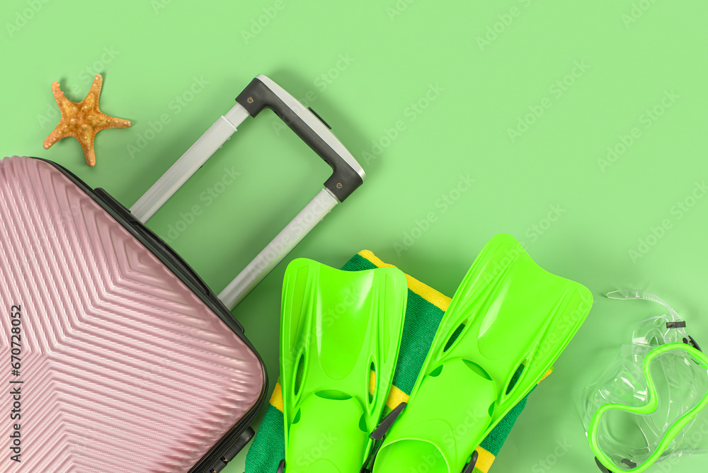 Suitcase, flippers and snorkeling mask on green background, closeup