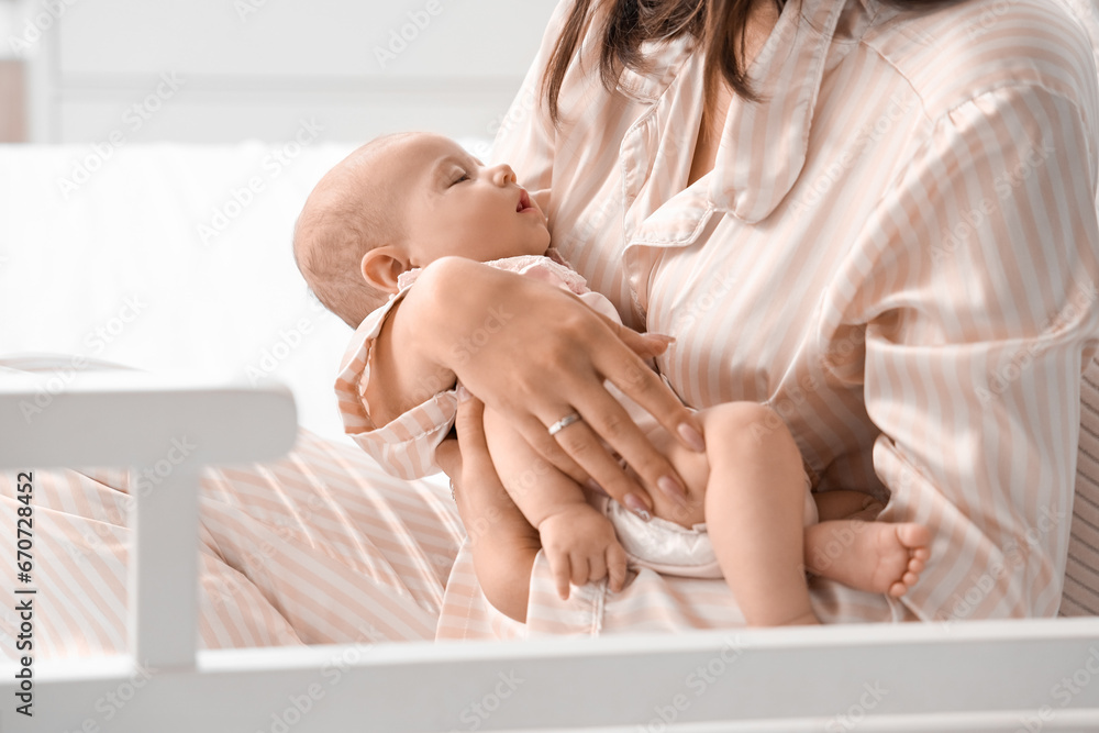 Happy mother with cute little baby sitting on bed in room